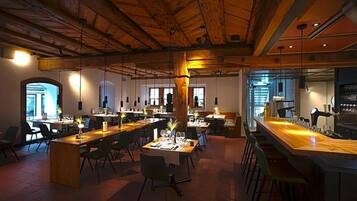Ein großzügiger Essbereich mit mehreren Tischen und Stühlen, Holzbalken an der Decke und einer Bar.