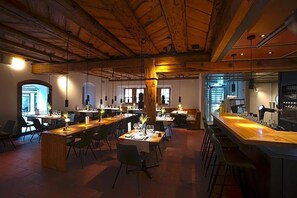 A spacious dining area with multiple tables and chairs, wooden beams on the ceiling, and a bar counter. - Gasthaus Zum Trauben (Weinfelden)