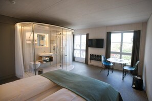 A modern hotel room with a bed, a glass-enclosed shower, a sink, a small table with chairs, a TV, and large windows. - Gasthaus Zum Trauben (Weinfelden)