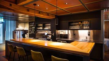 Eine Bar mit einer langen Holztheke, Barhocker und einer gut beleuchteten Decke mit Einbaustrahlern.