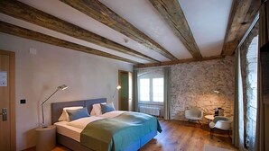 A bedroom with a wooden ceiling, stone wall, a bed with a green blanket, bedside lamps, a small table, and a chair. - Gasthaus Zum Trauben (Weinfelden)