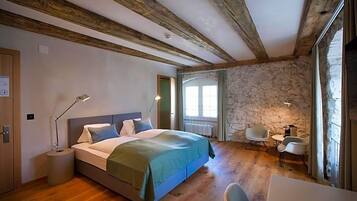 Ein Schlafzimmer mit Holzboden, Steinwand, einem Bett mit grüner Decke, Nachttischlampen, einem kleinen Tisch und einem Sessel.
