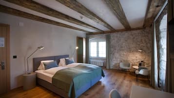 Ein Schlafzimmer mit Holzboden, einem Bett mit grüner Decke, einem Schreibtisch mit Stuhl und einer Steinwand.