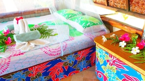 Ein Bett mit einer grün-weißen Bettdecke, ein Nachttisch mit einer Blumenvase und ein Fenster mit einem gewebten Rollo.