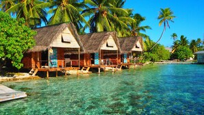 Overwater bungalows with thatched roofs, wooden decks, and clear blue water.