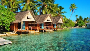 Overwater bungalows with thatched roofs, wooden decks, and clear blue water.