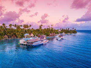 Ein tropisches Inselresort mit Bungalows über dem Wasser, einer Anlegestelle und einem im Wasser liegenden Boot.