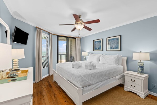 A bedroom with a bed, bedside tables, a ceiling fan, a TV, and a window with curtains. - Summer House 505 - Penthouse View! (Isle of Palms)