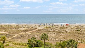 Una playa con cielo despejado, orilla arenosa y vegetación escasa.