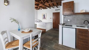 Eine kompakte Küche mit integriertem Geschirrspüler, ein Essbereich mit weißem Tisch und Korbstühlen sowie ein Schlafzimmer mit weißem Bett und einem Bild an der Wand.