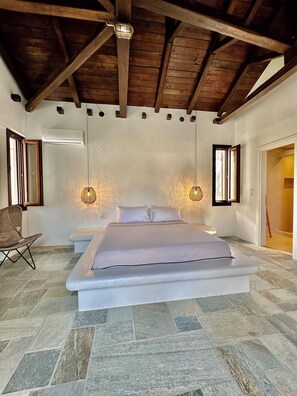 A bedroom with a large bed, wooden beams, stone flooring, and two wall-mounted lights. - Aeolos (Volos)