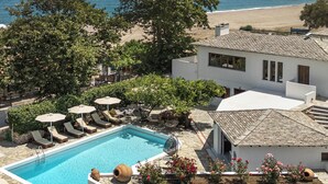 Ein Poolbereich mit Liegestühlen und Sonnenschirmen, mit Blick auf den Strand, und ein Gebäude mit einem Ziegeldach.