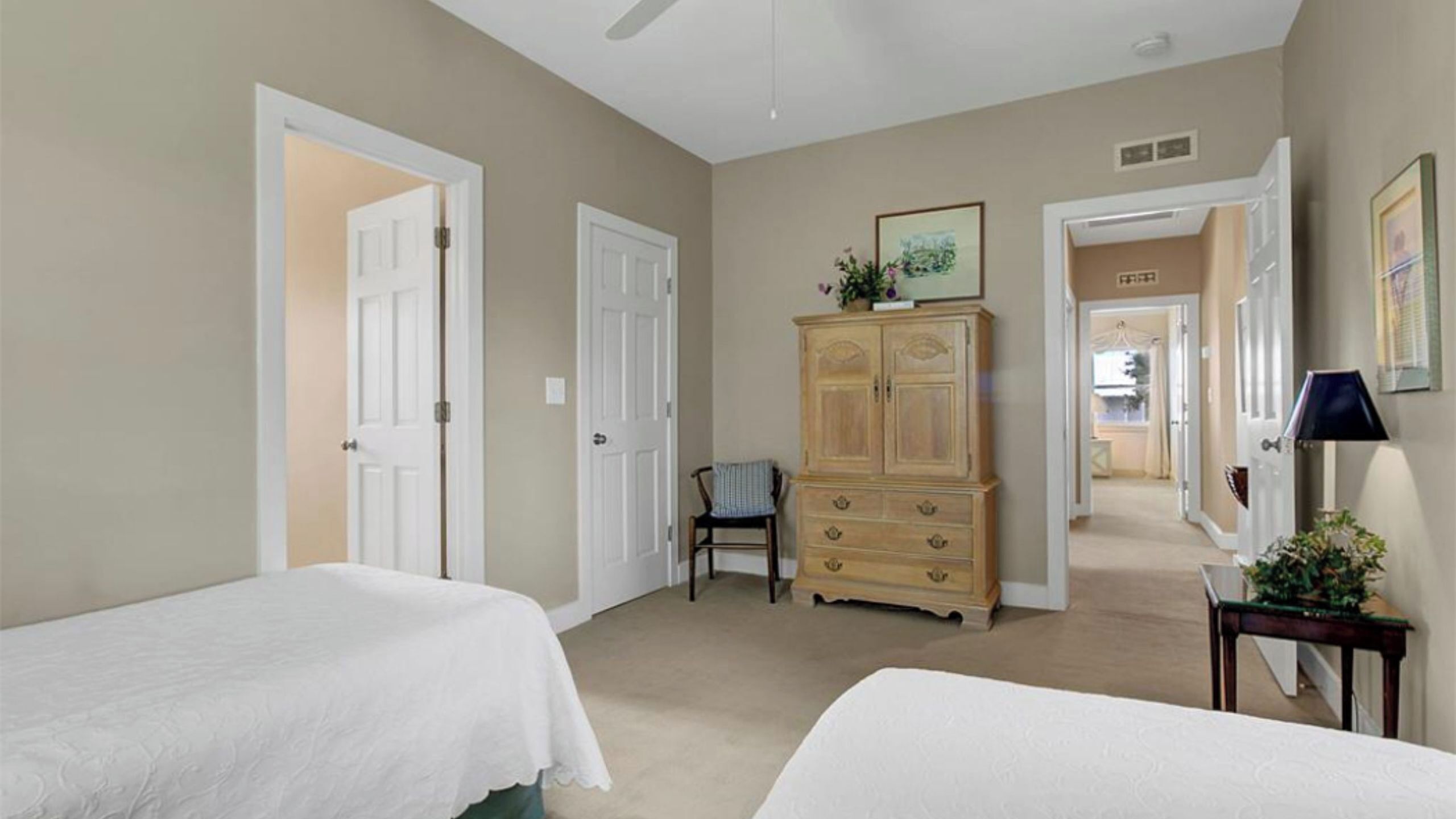 A bedroom with two beds, a wooden dresser, a chair, and a door leading to another room.