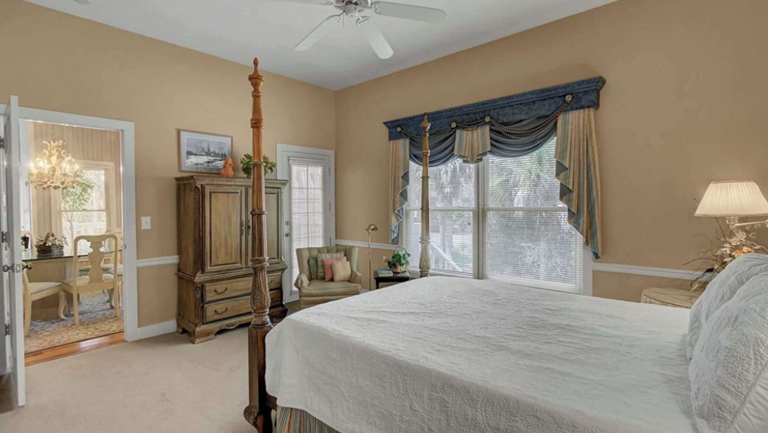 A bedroom with a bed, a wardrobe, a chair, a desk, a lamp, and a window with curtains.