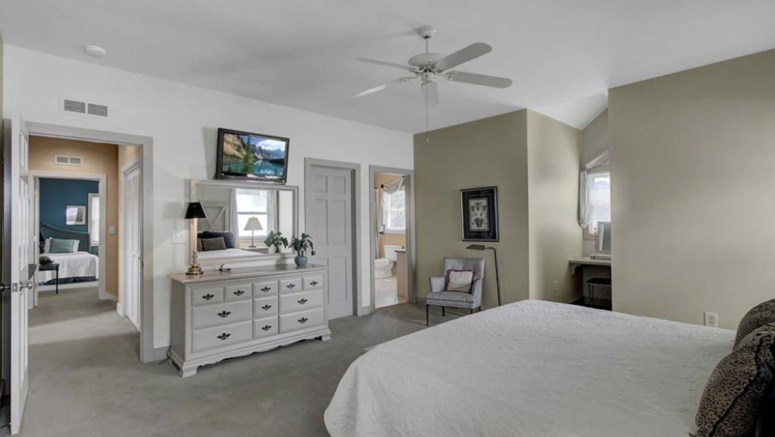 A bedroom with a bed, dresser, ceiling fan, and a bathroom door.
