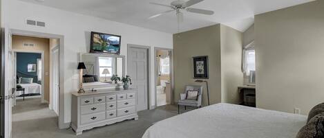 A bedroom with a bed, dresser, ceiling fan, and a bathroom door.