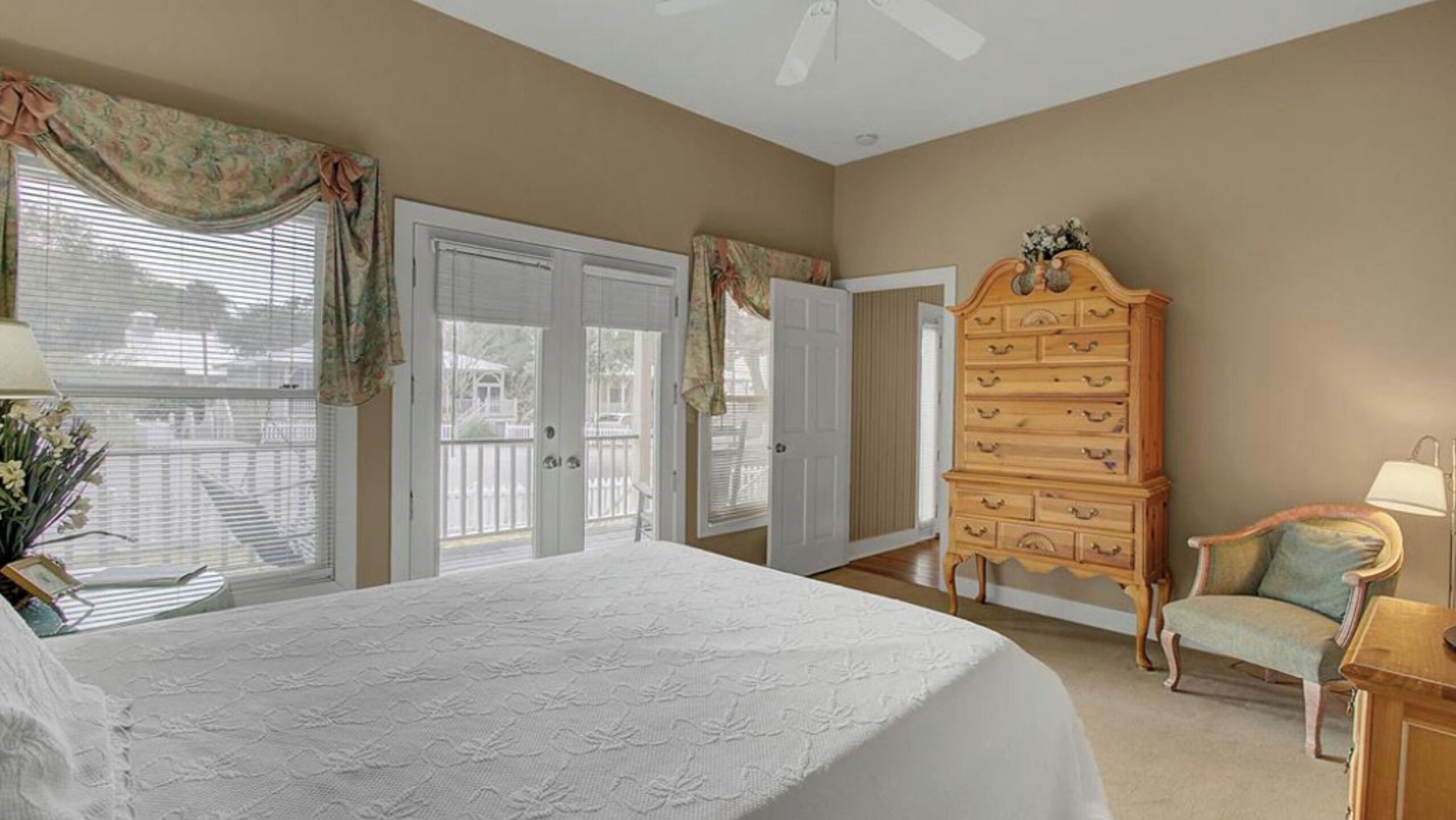 A bedroom with a bed, dresser, chair, and a view through the window.