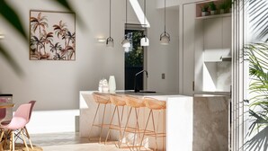 A modern kitchen with a bar area, pendant lights, and a large window. - Meli Beach House by Experience Jervis Bay (Callala Beach)