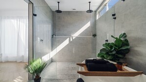 A modern bathroom with a glass shower enclosure, a wooden vanity, and a large green plant. - Meli Beach House by Experience Jervis Bay (Callala Beach)