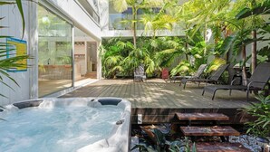 A hot tub, lounge chairs, and a wooden deck with tropical plants. - Meli Beach House by Experience Jervis Bay (Callala Beach)