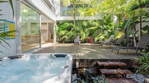 Uma banheira de hidromassagem, espreguiçadeiras e um deck de madeira com plantas tropicais.
