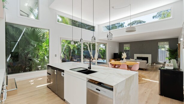 A modern kitchen with a large island, built-in dishwasher, and a dining area with a wooden table and chairs. - Meli Beach House by Experience Jervis Bay (Callala Beach)