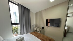 A hotel room with a bed, a desk, a chair, a TV, and a window with curtains. - Bela Hospedagem - 105 Solaz Smart (João Pessoa)