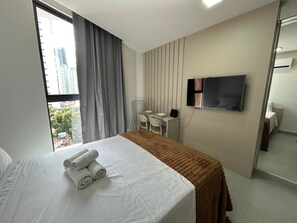 Ein Hotelzimmer mit Bett, Schreibtisch, Stuhl, Fernseher und einem Fenster mit Vorhängen.