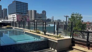 A rooftop pool with a city view, lounge chairs, and a clear sky.