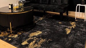 A room with a black sofa, a round coffee table, and a black and gold rug.