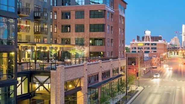 A multi-story building with a glass facade, a pedestrian bridge, and a street view.