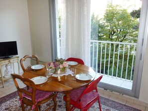 Uma mesa de jantar com cadeiras, um vaso de flores e uma televisão em um suporte.