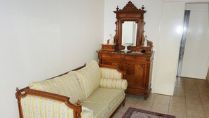 A room with a wooden sofa, a wooden dresser with a mirror, and a patterned rug. - Bouchardon (Paris)
