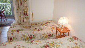 A room with two beds, a small table with a lamp, a chair, a window with curtains, and a hanging decorative item. - Bouchardon (Paris)