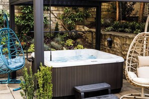 A hot tub in a covered outdoor area with wicker chairs and a stone wall. - Dukes Hotel (Bath)