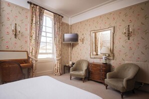 A hotel room with a bed, two armchairs, a wooden desk, a television, a mirror, and a dresser. - Dukes Hotel (Bath)