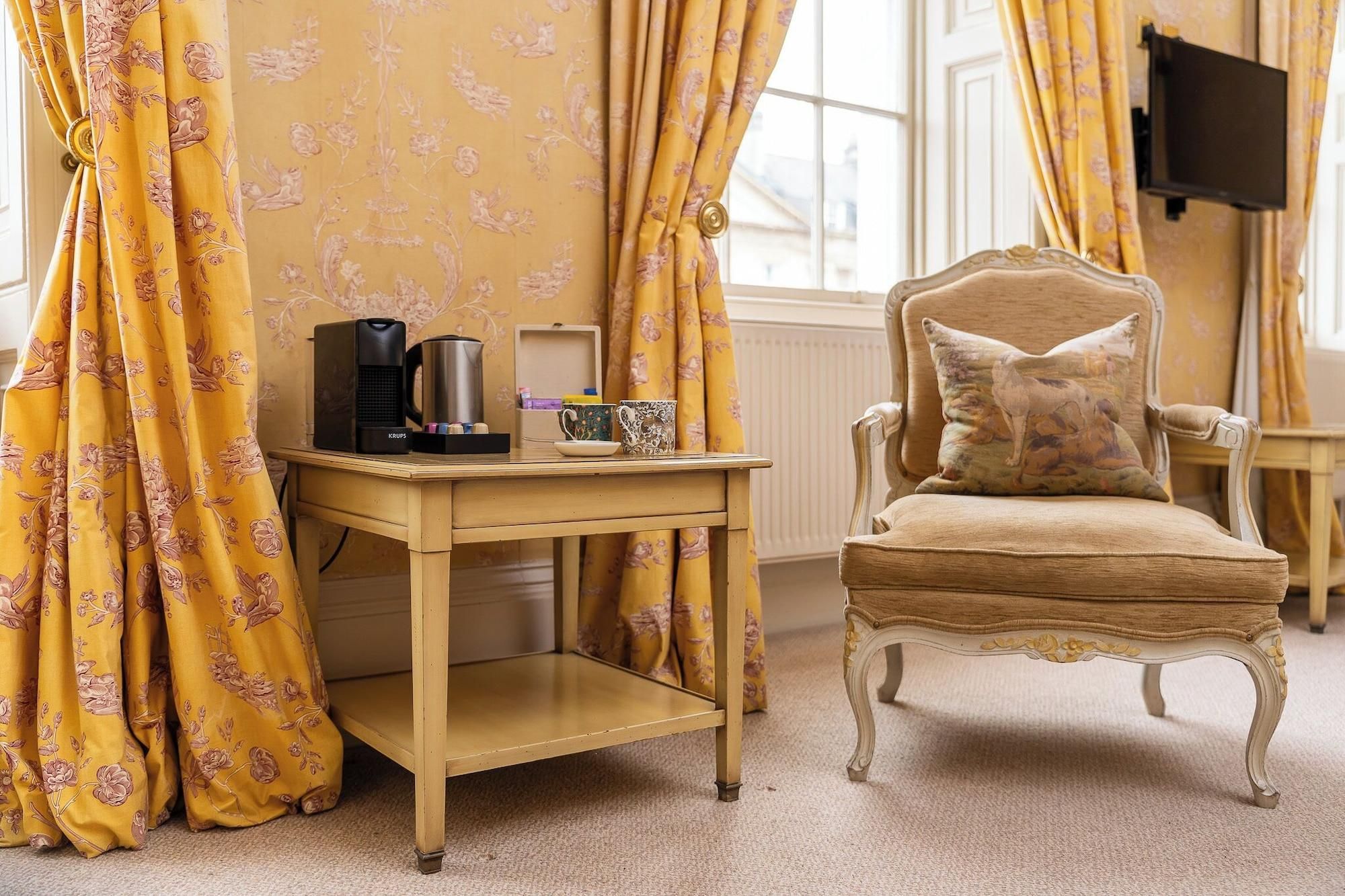 A room with a wooden table, a chair, a coffee maker, and a television.
