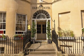 A hotel entrance with a sign reading 'Duke Hotel,' a set of stairs leading up to the door, and a wrought iron fence surrounding the property. - Dukes Hotel (Bath)