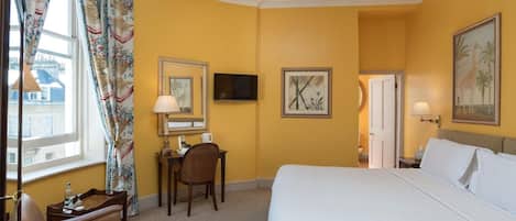 A hotel room with a bed, a desk, a chair, a TV, and a door leading to a bathroom.