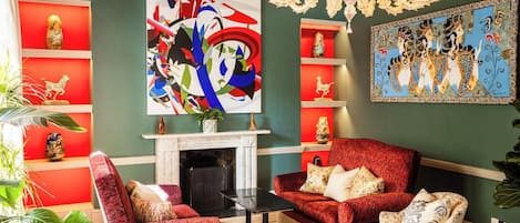 Uma sala de estar com lareira, móveis vermelhos e brancos e objetos decorativos nas prateleiras.