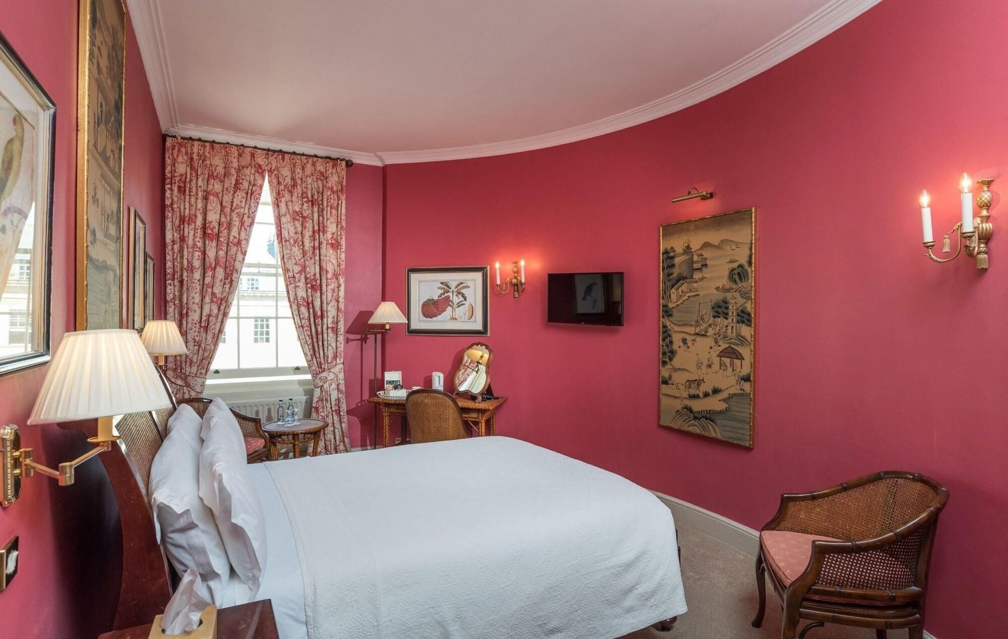 A hotel room with a bed, a desk, a chair, a television, and artwork on the walls.