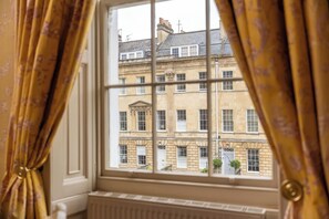 A window with a view of a multi-story building with a classical architectural style, featuring a central column and a symmetrical facade. - Dukes Hotel (Bath)