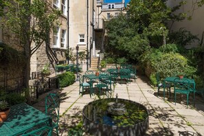 An outdoor patio with green metal tables and chairs, a central fountain, and surrounding greenery. - Dukes Hotel (Bath)