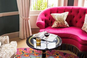 A room with a pink sofa, a small round table with a glass of wine, and a patterned rug. - Dukes Hotel (Bath)