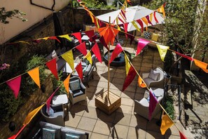 Terrassa exterior amb mobiliari de vimet, un arca de fusta i banderes triangulars de colors.