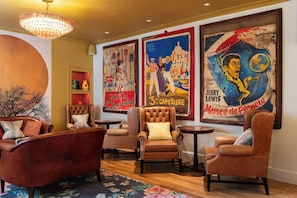 A lounge area with leather armchairs, a chandelier, and vintage posters on the wall.