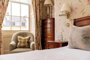 A bedroom with a bed, a wooden dresser, a lamp, and floral wallpaper. - Dukes Hotel (Bath)