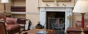 A room with a fireplace, leather armchairs, a table with a book, and a bookshelf with books. - Dukes Hotel (Bath)