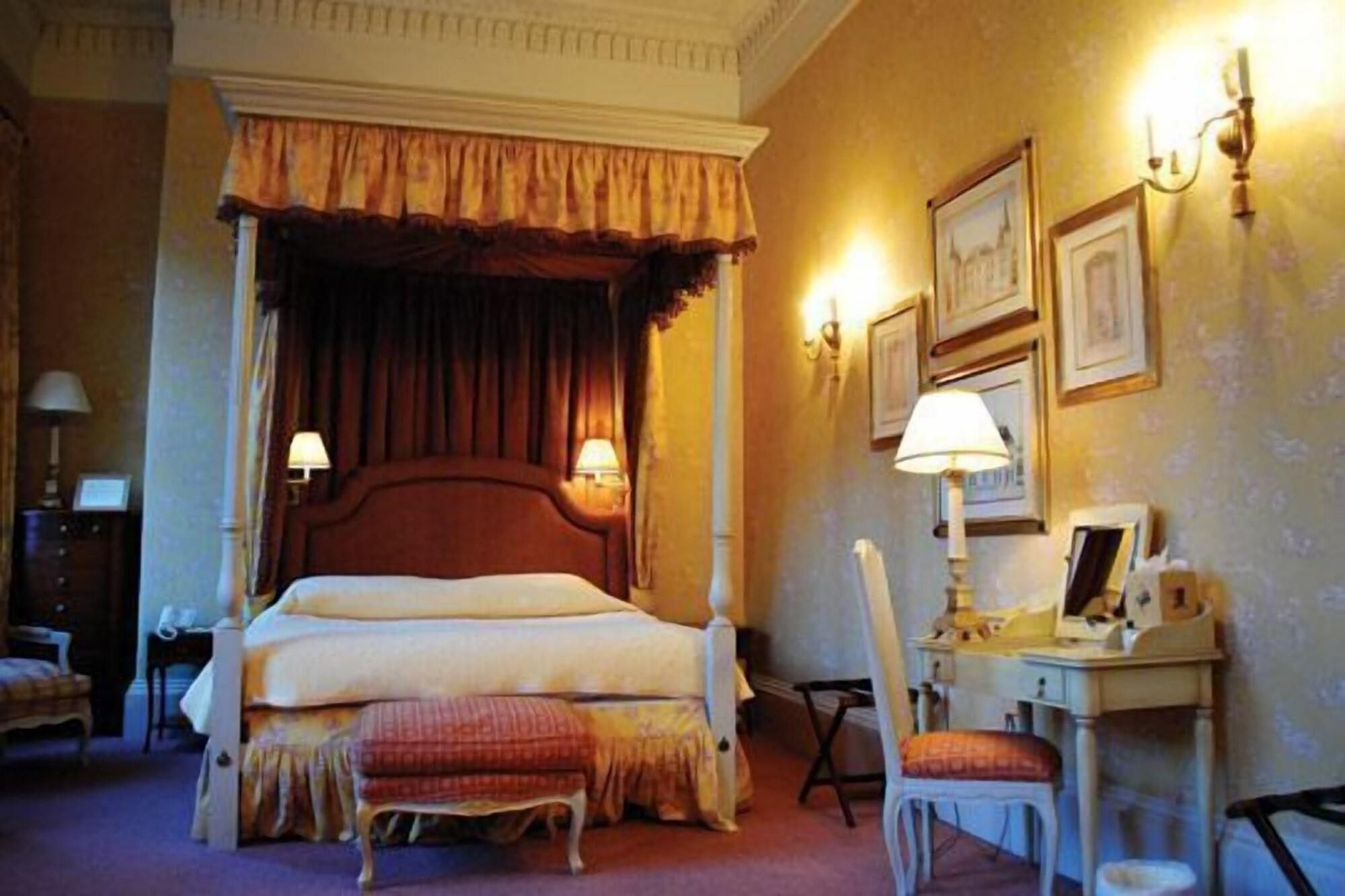 Een hotelkamer met een hemelbed, een bureau met een stoel en een kleine tafel met een lamp.