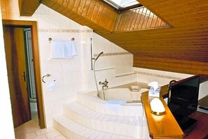 Un baño con bañera, ducha, tocador de madera y tragaluz.